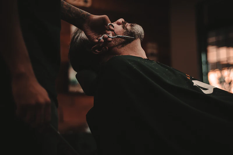 Barbero perfilando con tijera el cabello de un cliente reclinado